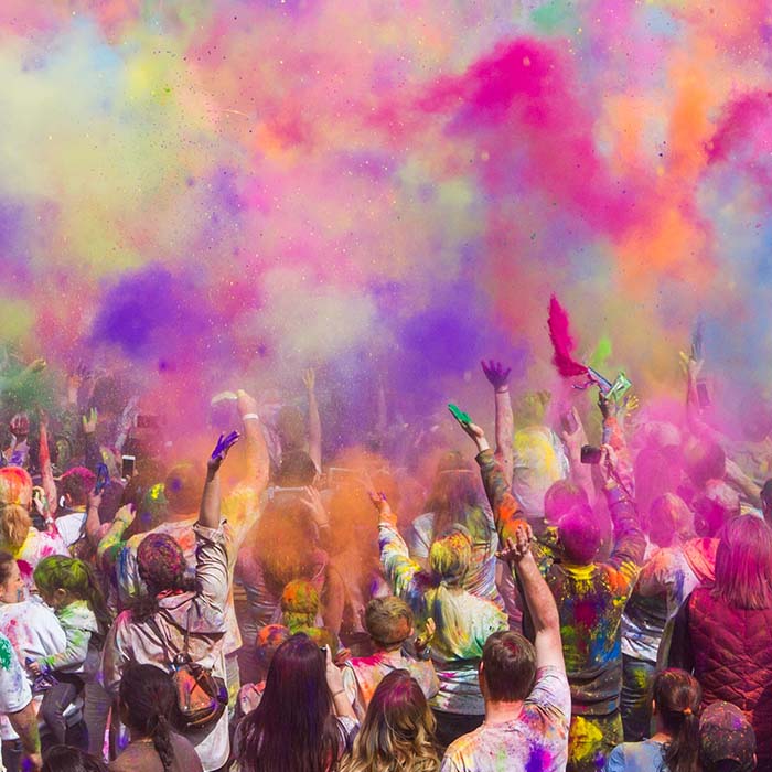 crowd of people throwing multiple different coloured powders into the air